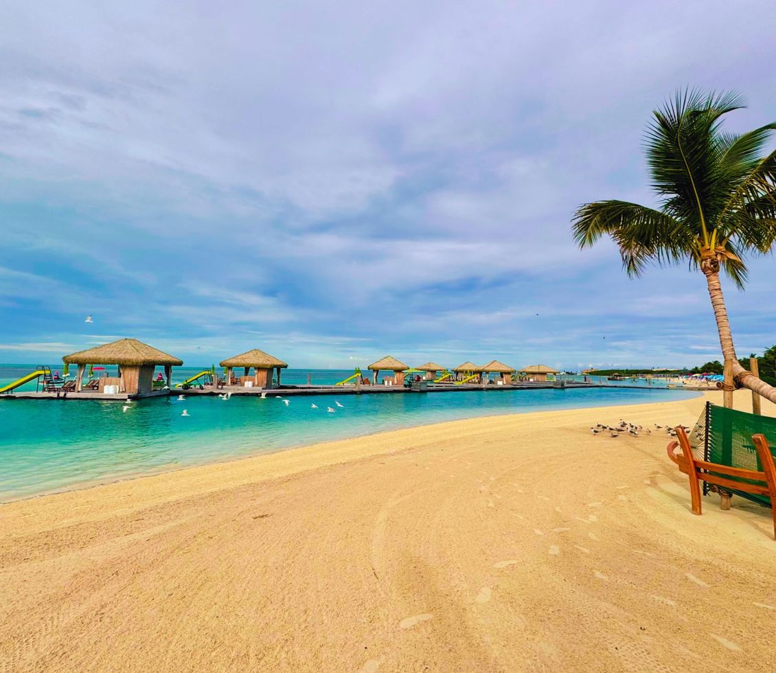 A strip of golden sand and overwater cabanas at Coco Beach Club of CocoCay. 